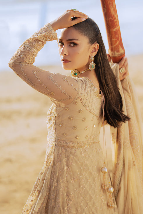 Model wearing full NAQSHI Alara 3PC set: skin‑beige net frock with hand‑embroidered tiers, heavy back tassels, plain straight PK raw‑silk pants and embellished dupatta.