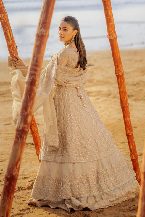 Model wearing full NAQSHI Alara 3PC set: skin‑beige net frock with hand‑embroidered tiers, heavy back tassels, plain straight PK raw‑silk pants and embellished dupatta.