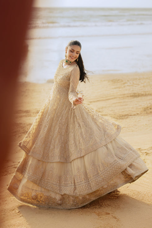 Model wearing full NAQSHI Alara 3PC set: skin‑beige net frock with hand‑embroidered tiers, heavy back tassels, plain straight PK raw‑silk pants and embellished dupatta.