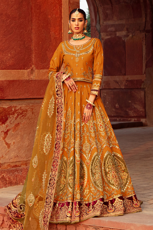 Naqshi Zarwisha mustard raw‑silk boat‑neck choli richly embroidered with dori and tilla, full sleeves, paired with matching heavy‑embroidered lehenga featuring velvet applique border and tie‑dye dupatta.