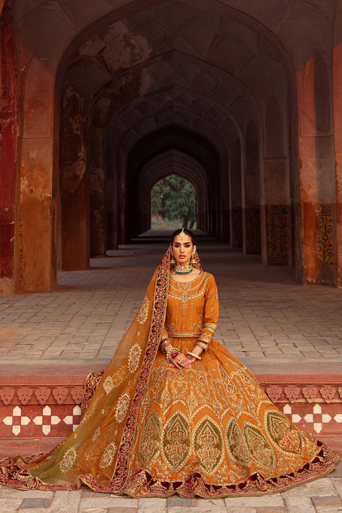 Model wearing full Zarwisha set: mustard boat‑neck choli, embroidered lehenga with velvet border & tie‑dye dupatta styled for bridal elegance.