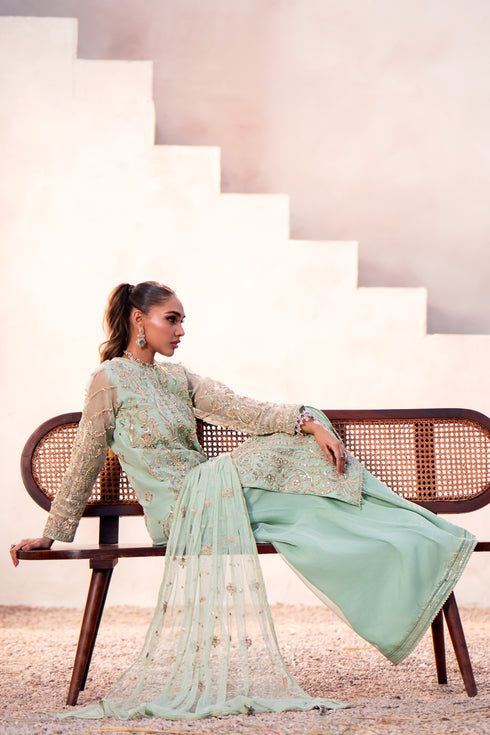Model wearing full Naqshi Parsa 3PC set: aqua organza shirt with hand‑adda embellishments, sharara and embroidered dupatta styled for festive elegance.