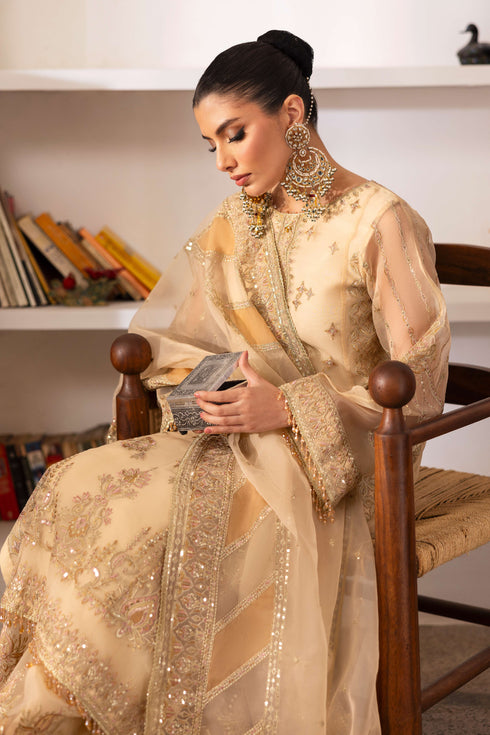 Model wearing NAQSHI Marve seated, highlighting shirt’s embroidered neckline, crystal tassels, star motifs, contrasted by sharara and draped dupatta.