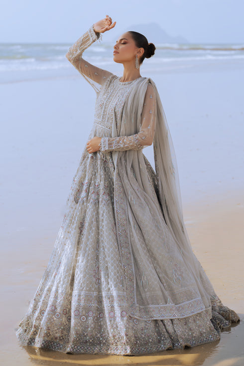 Side profile of NAQSHI Valeria showcasing the flow of silver net frock, layered sequin and floral embroidery on bodice extending to sleeves, and plain straight PK raw‑silk pants.