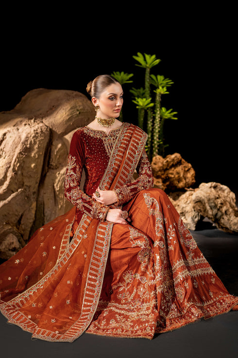 Seated pose of NAQSHI Amber rust orange outfit showing wide sharara panels and organza dupatta border