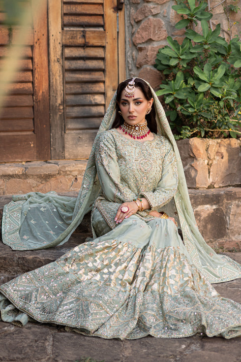 Model seated in Mah‑e‑Meer 4PC set showcasing raw‑silk shirt, gypsy gharara layers, bejeweled dupatta and potli bag for dreamy nikkah styling.