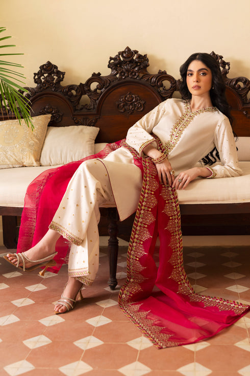 Model wearing full NAQSHI Abish 3PC set: embellished white raw‑silk shirt with V‑neck hand‑adda work, sequin-sprayed culottes & contrasting hot‑pink organza dupatta for a striking look.