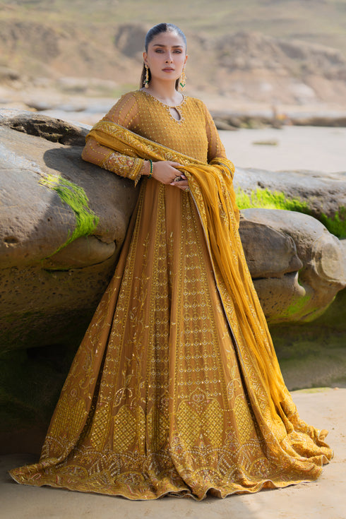 Model wearing full NAQSHI Ainara 3PC set: mustard crinkle frock with keyhole neck, hand‑adda panels and tassels, paired with plain straight pants and embroidered dupatta.