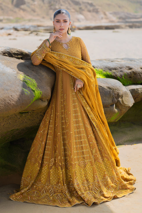 Model wearing full NAQSHI Ainara 3PC set: mustard crinkle frock with keyhole neck, hand‑adda panels and tassels, paired with plain straight pants and embroidered dupatta.