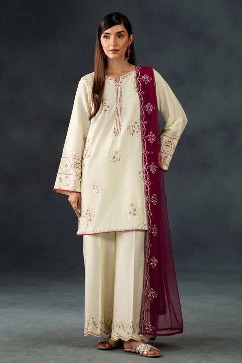 Woman wearing a cream embroidered outfit with a maroon dupatta against a dark background