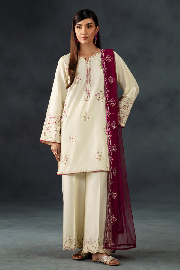 Woman wearing a cream embroidered outfit with a maroon dupatta against a dark background