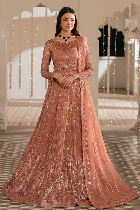 Woman in a traditional pink embroidered outfit standing in an elegant indoor setting.