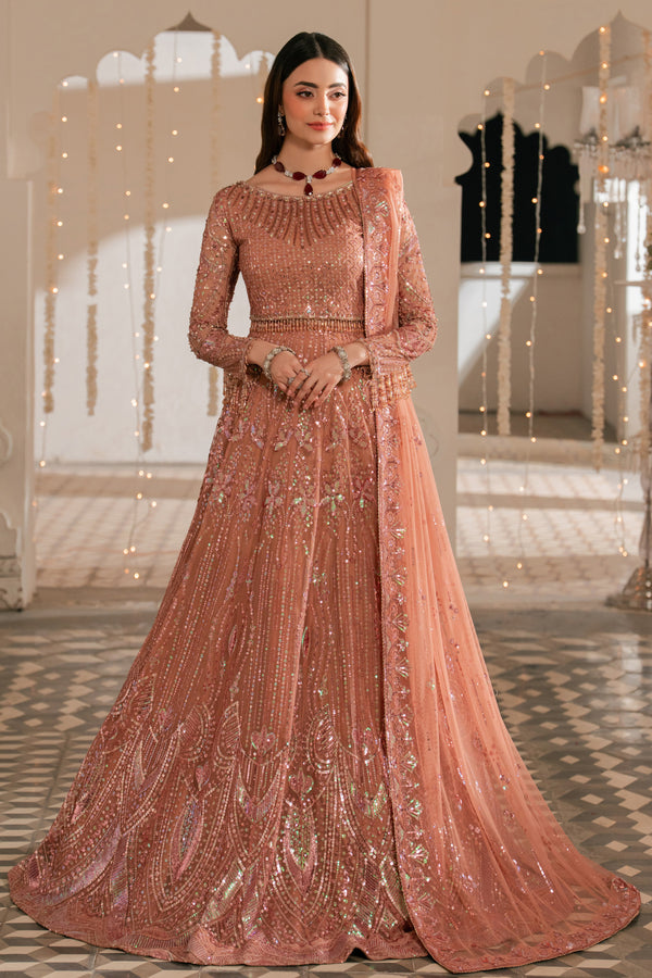 Woman in a traditional pink embroidered outfit standing in an elegant indoor setting.
