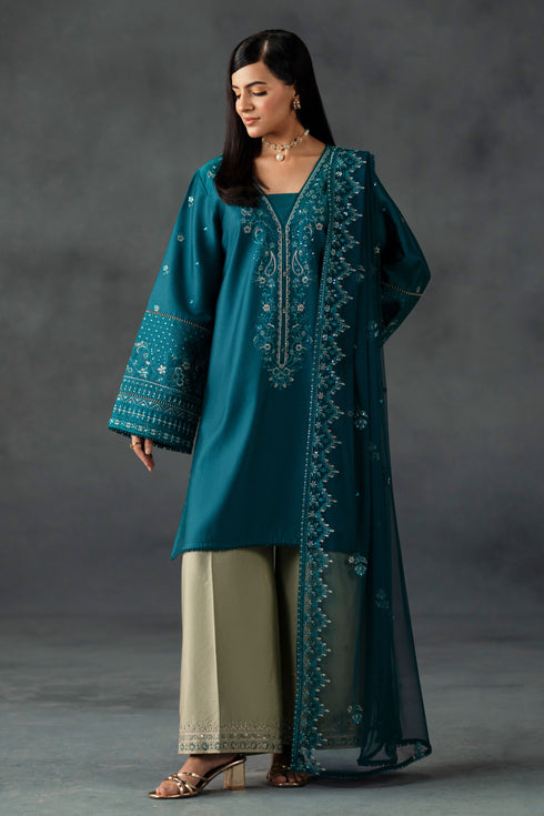 Woman wearing a teal embroidered outfit against a gray background