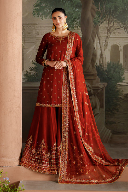 Woman in a red traditional outfit with gold embroidery standing in an outdoor setting.