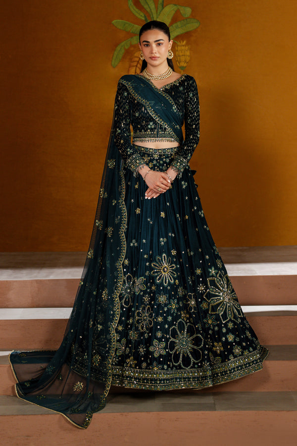 Woman in a dark blue embroidered traditional outfit against an orange wall.