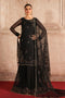 Woman in a black embroidered traditional outfit with a sheer dupatta against a beige wall.