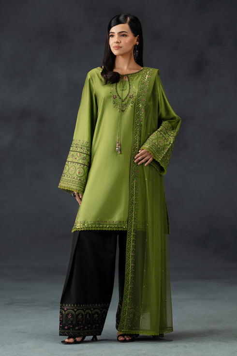 Woman wearing a green embroidered outfit with black pants against a gray background