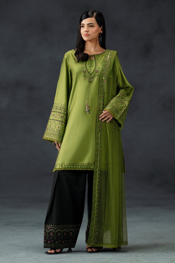Woman wearing a green embroidered outfit with black pants against a gray background