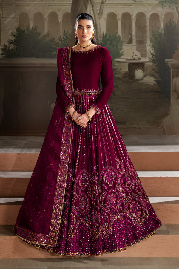 Woman in a maroon embroidered traditional outfit standing on steps with a classical architecture background.
