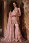 Woman in a traditional pink embroidered outfit standing against an ornate wall.