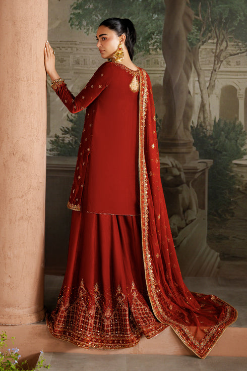 Woman in a traditional red outfit with gold details standing against an architectural background.
