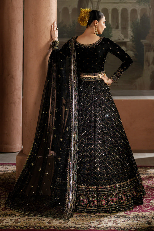 Woman in a black embroidered traditional outfit standing in a decorated room.