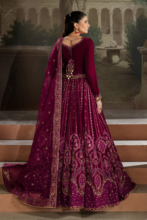 Woman in a traditional maroon embroidered outfit standing on steps with a decorative background.