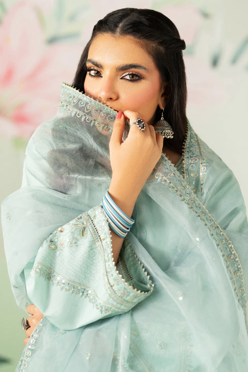Woman wearing a light blue embroidered saree with a blurred floral background