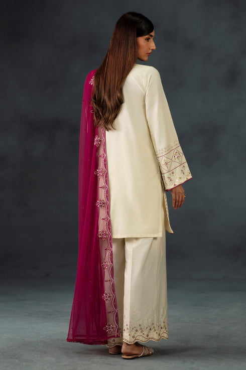 Woman in traditional cream outfit with pink dupatta against a dark background