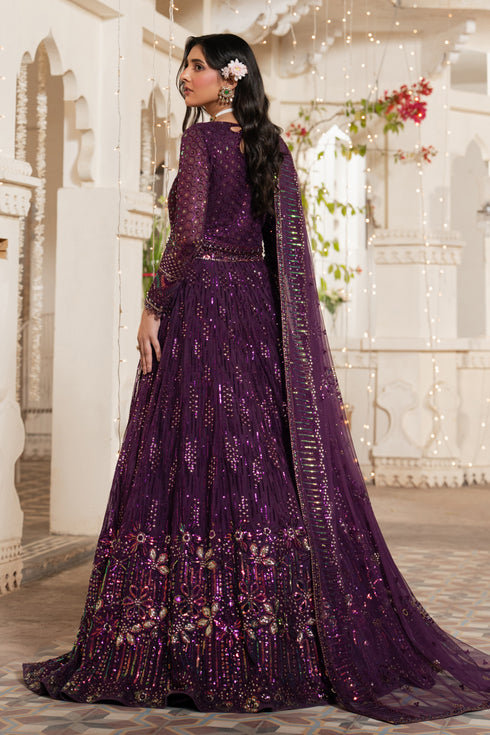 Woman in a purple embroidered traditional outfit standing in an elegant indoor setting.