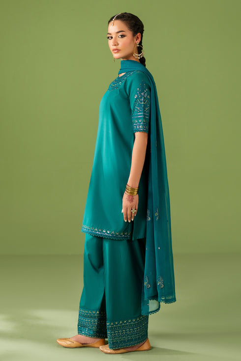 Side standing view of NAQSHI Ruhab outfit highlighting clean shirt cut, embroidered trouser border, and relaxed silhouette