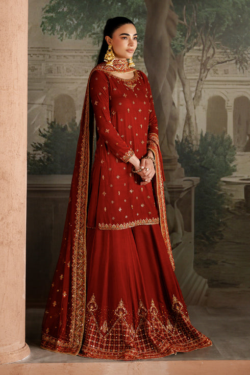 Woman in a traditional red embroidered outfit standing in an outdoor setting with classical architecture.