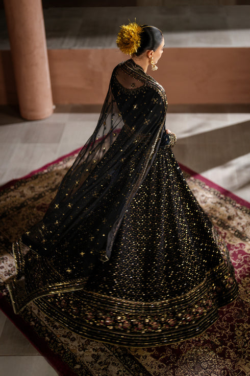 Woman in a black embroidered traditional outfit sitting on a patterned rug.