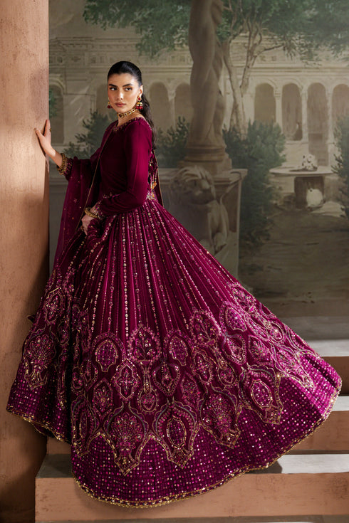 Woman in a vibrant purple traditional outfit with intricate patterns, standing against an artistic backdrop.