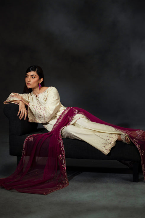 Woman in a white blouse and maroon saree sitting on a black chair against a dark background