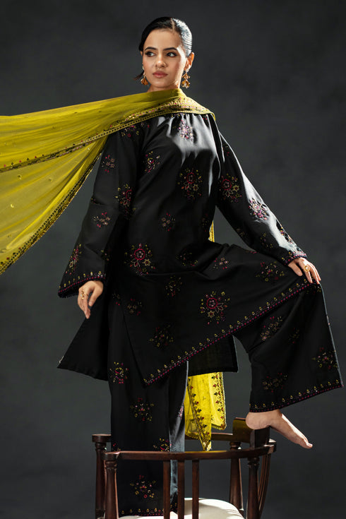 Woman in a black traditional outfit with yellow dupatta against a dark background