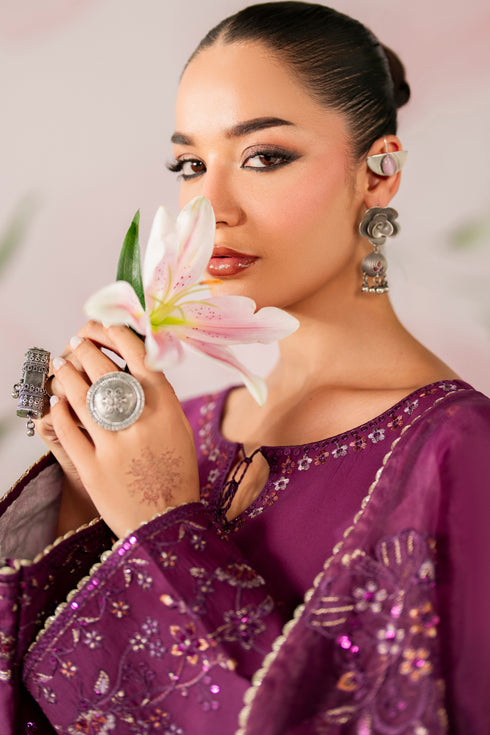 Woman in a purple traditional outfit holding a white flower with a blurred background