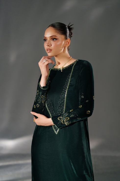 Woman wearing a dark green dress with gold embellishments against a gray background