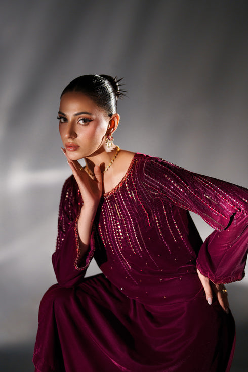 Woman in a burgundy dress with sequin details posing against a gray background