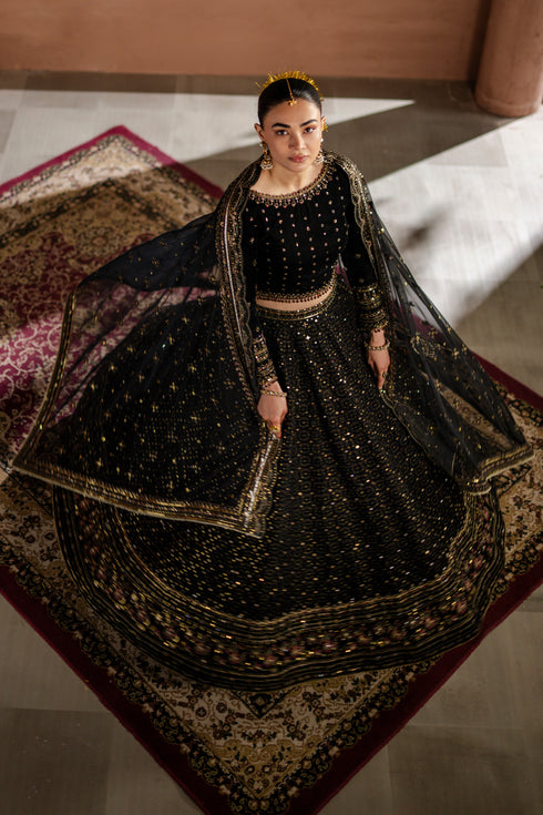 Woman in a black traditional outfit with gold details on a patterned rug.