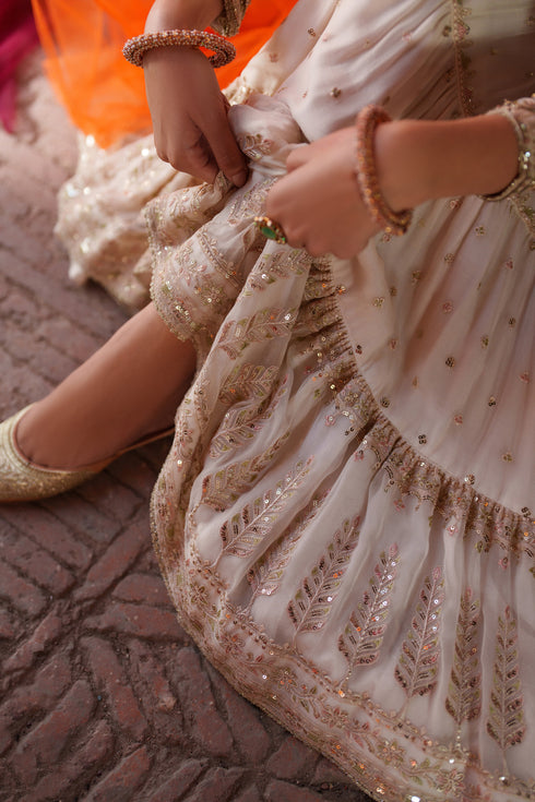 Close-up of a person wearing a beige embroidered dress with gold details on a textured surface.