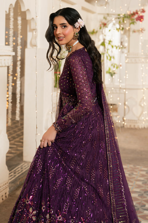 Woman in a purple embroidered traditional outfit standing in a decorated indoor setting.