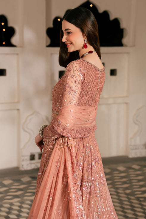 Woman in a pink embroidered outfit standing in an elegant interior setting.