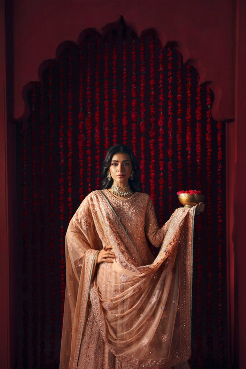 Model wearing NAQSHI Ashiayana peach 3-piece set: frock with embroidery, matching trousers and net dupatta