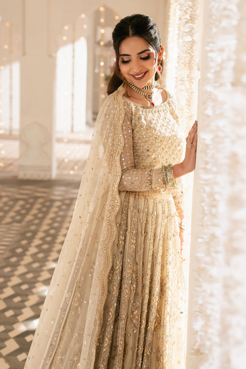 Woman in a traditional outfit with a gold and white theme, standing indoors.