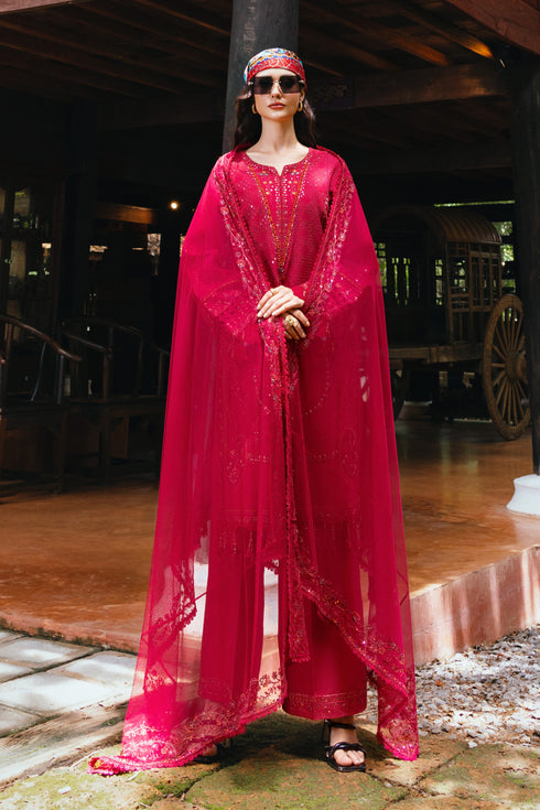 Woman in a vibrant pink traditional outfit with a headscarf, standing outdoors.