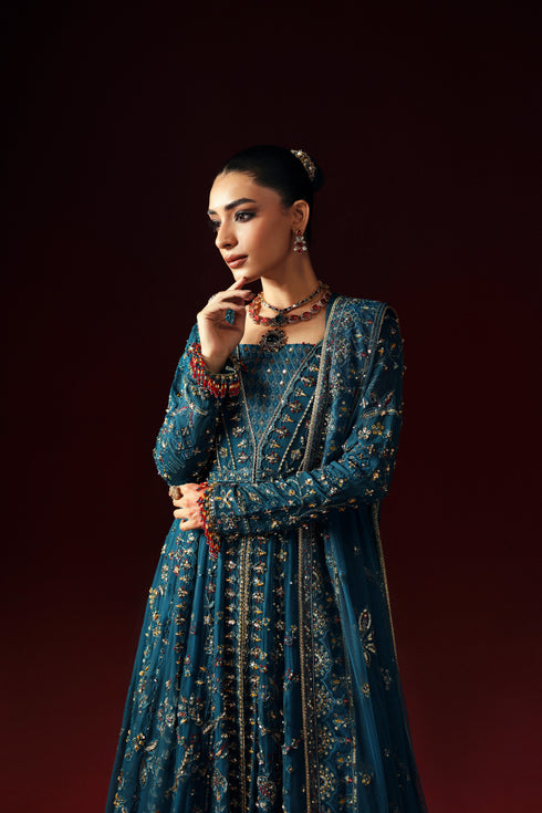 Woman wearing a blue embroidered traditional outfit with jewelry against a dark background