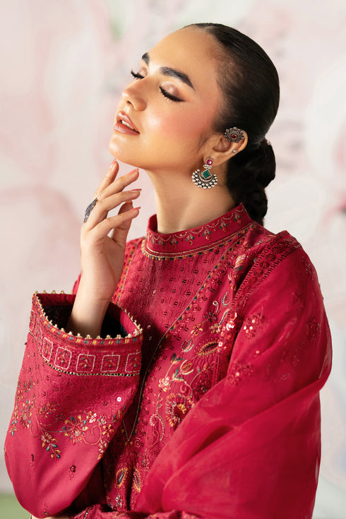 Woman wearing a red embroidered traditional outfit with a soft pink background