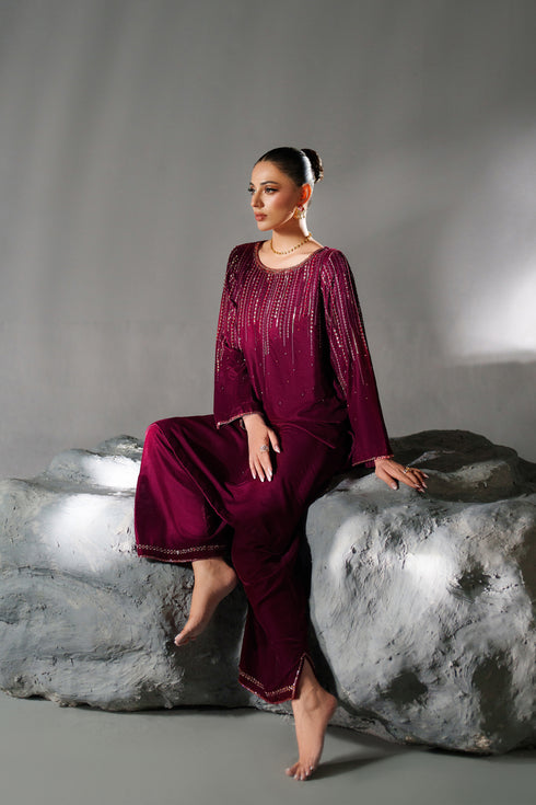 Woman in a burgundy outfit sitting on a rock against a gray background